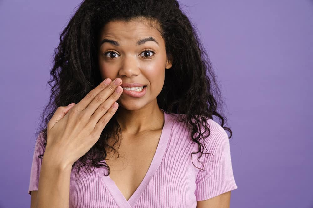 Young black woman covering her mouth while expressing surprise isolated over purple background