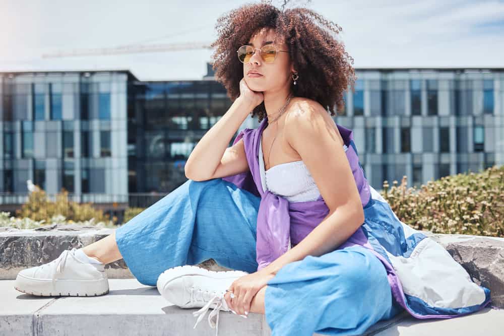 A stylish African American lady with curly fine hair shafts that are dark brown natural color is relaxing on a summer day.