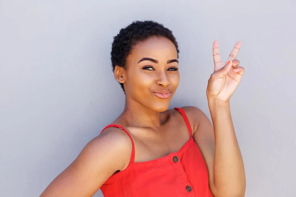 Cute black girl that's saying goodbye with a peace sign hoping to wear a dutch braid hairstyle.