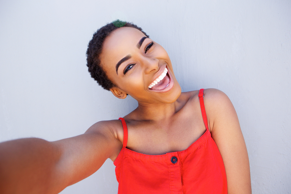 A cute young African American female with shorter hair is wearing a fun and casual look with a red shirt.