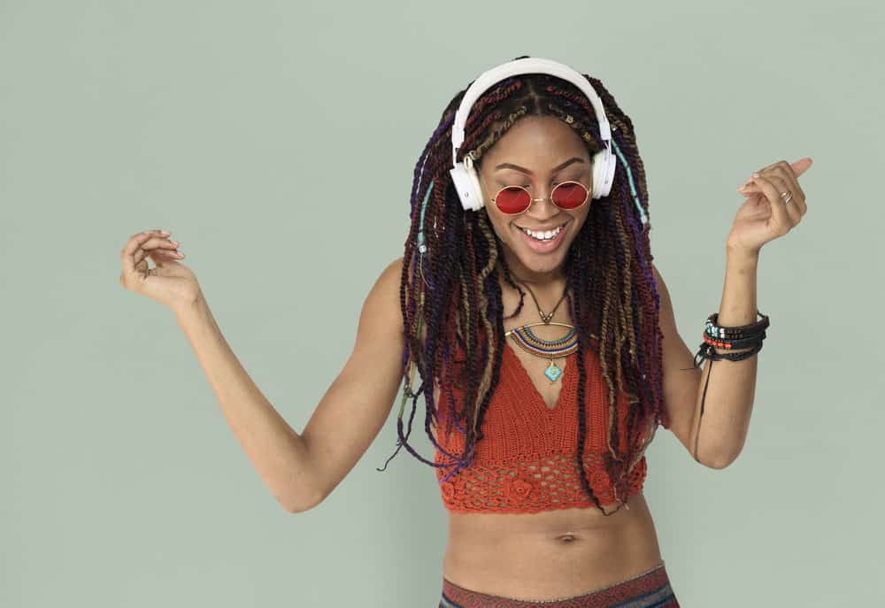 A young black girl with long braids wearing an orange casual shirt while listening to headphones and dancing. 
