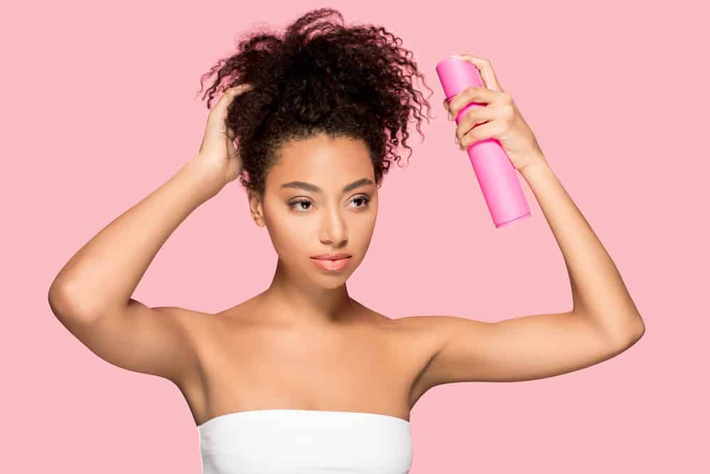 African woman using an aloe spray that's about to plop curly hair with a short-sleeve t-shirt.