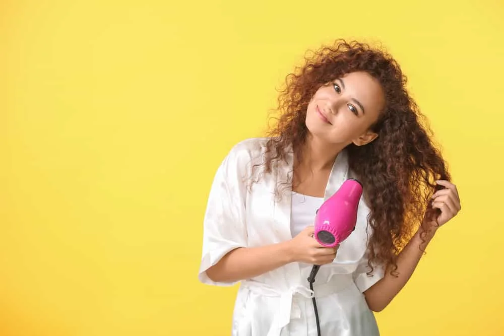 A cute young black female with thick hair using a hair dryer with adjustable heat settings and variable heating element.