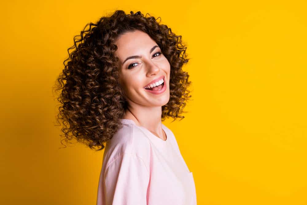 A white girl with flat iron permed hair created with normal hair styling techniques looks back at the camera.