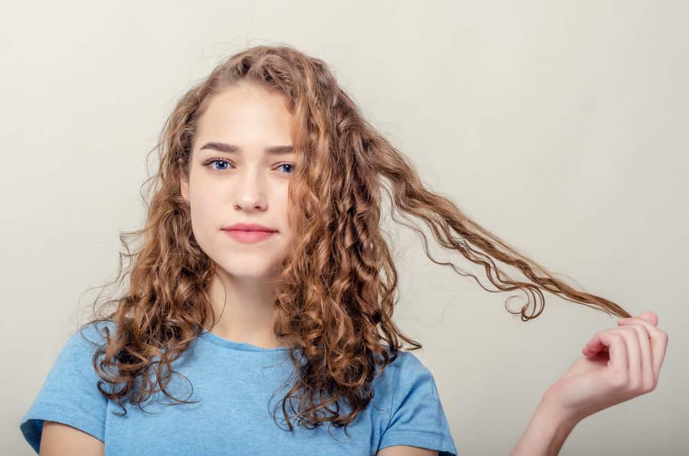 A female with blue eyes wearing red lipstick with coily hair styled with curl creams and a coconut oil styling product.