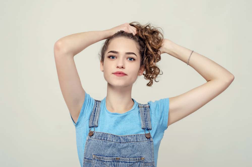 An attractive girl with densely packed waves is preparing to pineapple her hair for tighter curls.