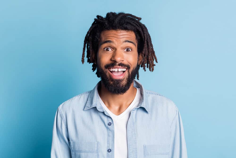 Attractive young guy with a deep side parting on mature 4C dreadlocks wearing a blue jean dress shirt.
