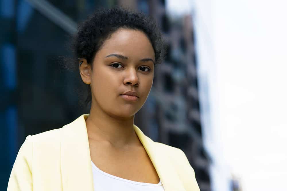 An African American female, after drying her wet hair with a hair dryer, tied up her hair completely with a rubber tie.