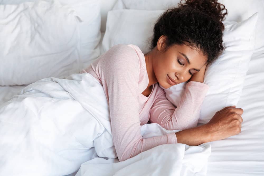 A young female with long hair styled with curl cream has been tied up in a loose bun as she prepares to fall asleep.