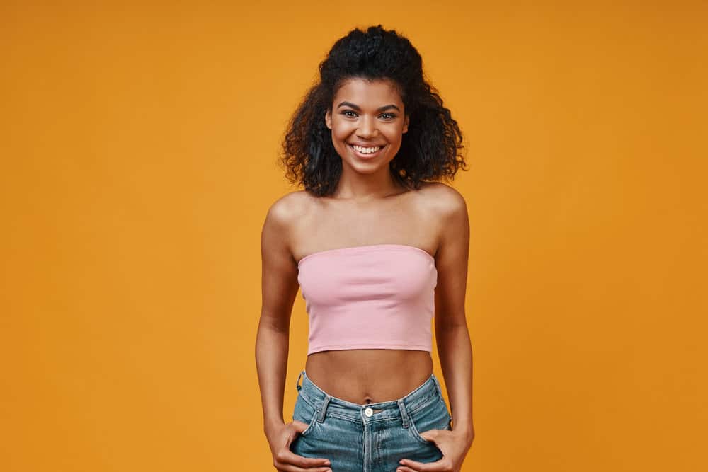 A cute young black lady wearing curly hair extensions due to deep splits on her hair ends from excessive heat styling.
