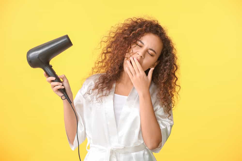 A sleepy African American female holding one of the newer tourmaline hair dryers while drying her brittle hair.