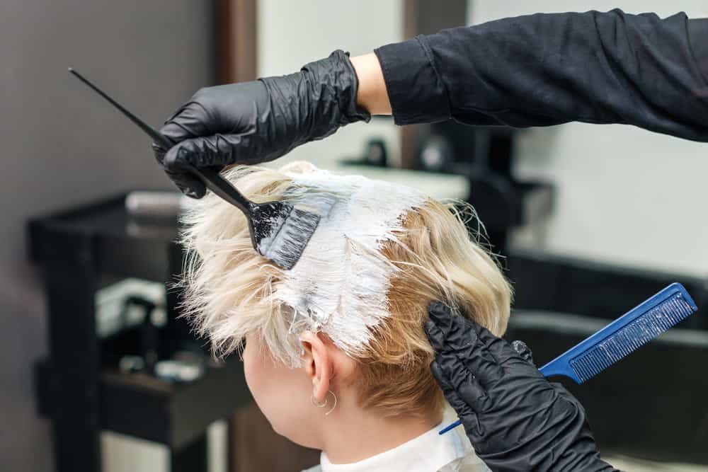Hairdresser applying modern hair dye to a client while carefully trying to avoid stubborn stains and dyed skin.