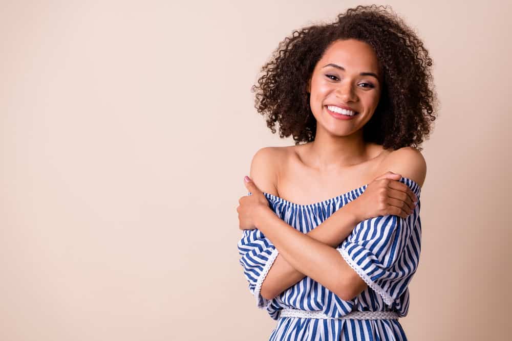 Light skinned black girl embracing herself with dark hair after using a no lift hair color in her natural curls.