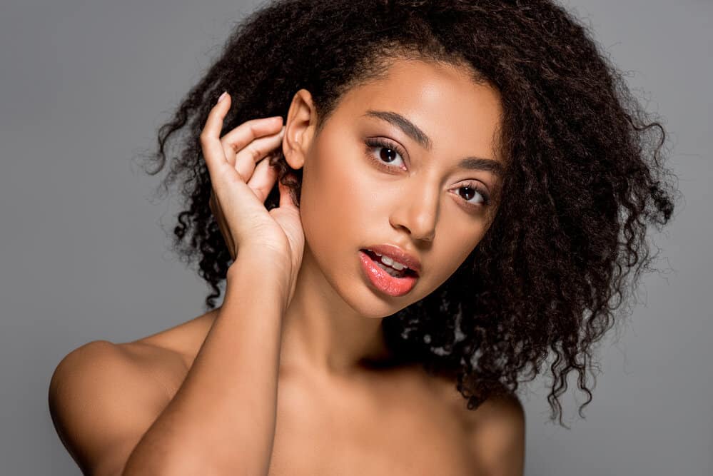 A young black girl with bouncy curls on 3B fine hair strands prepping to her thicker hair plopped with a towel turban.