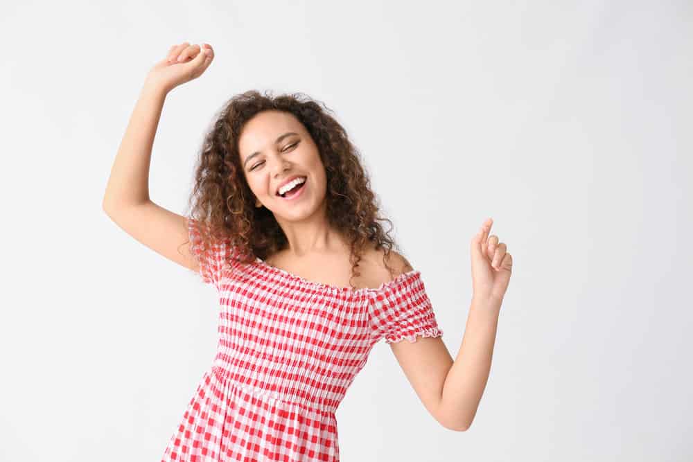 A happy young lady with high porosity hair is enjoying her frizz-free springy curls using a curl-centric hair care routine.