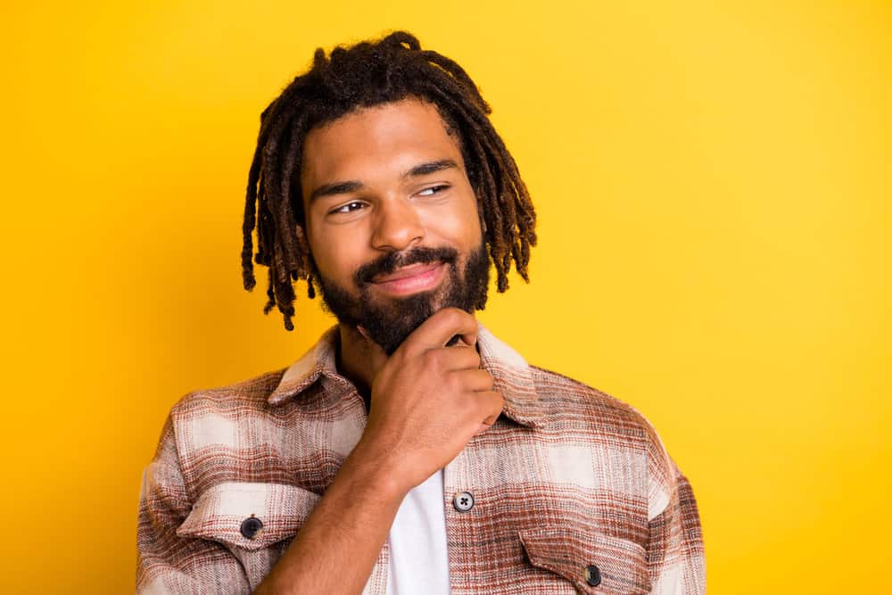 A man with wide shoulders wearing mature dreadlocks with light brown tips and a plaid shirt.