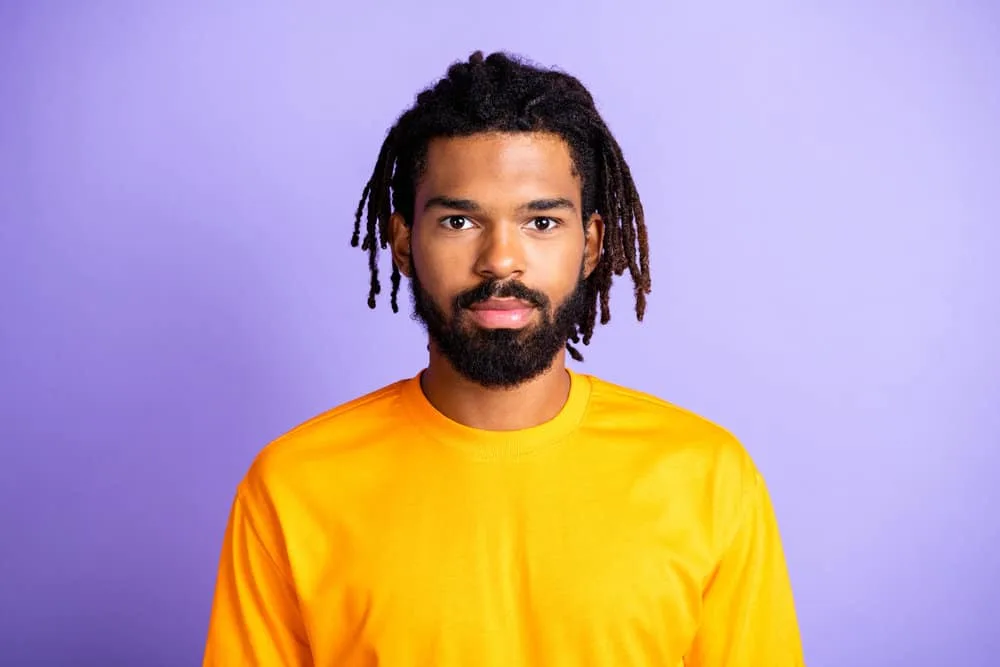 African American male wearing a yellow t-shirt with a dark brown beard and two strand twist braids with brown tips.