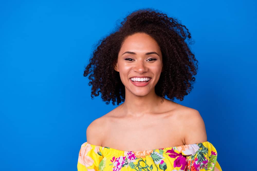 A cute young black girl with natural curls has a smoothing treatment on her 3C frizzy hair strands.