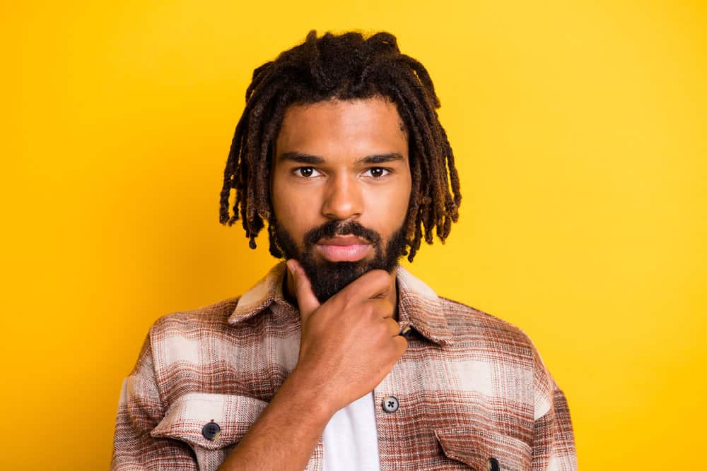 A bearded man with natural curls in a loc hairstyle with subtle bleach on the tips to create a light brown color.