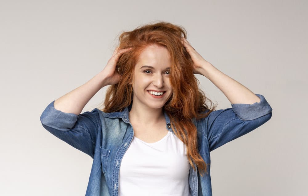 Caucasian female smiling and touching her type 2B hair strands as she determined how to style her natural waves.