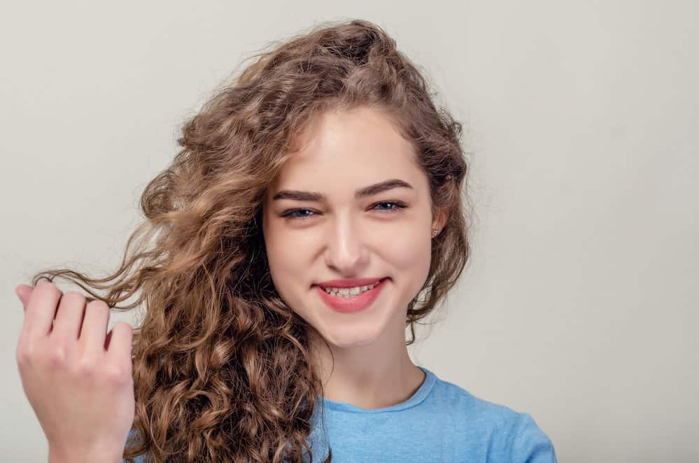 A cute female with a wavy curl type has dry hair treated with leave-in conditioners on wash days.