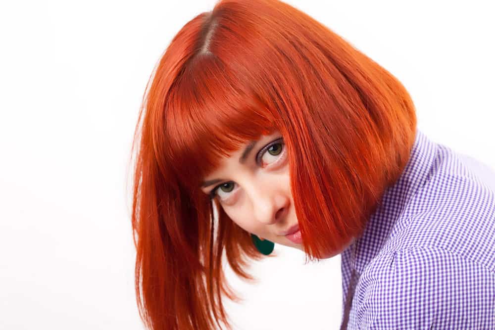 A lady wearing a darker shade of red hair color with a purple and white checkboard dress shirt.