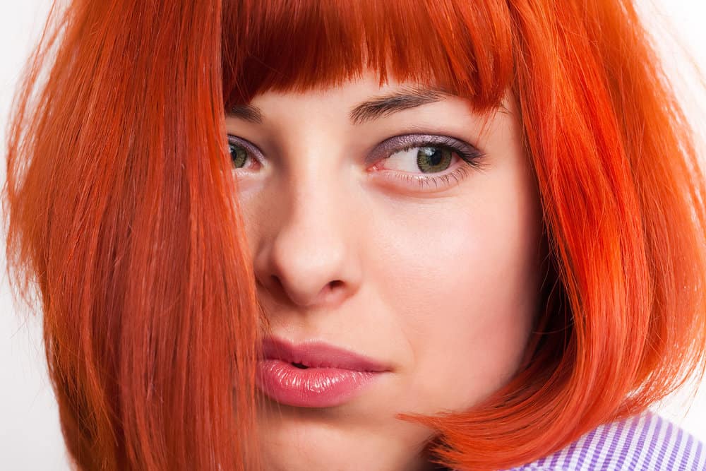 A woman wearing bright colors on her hair, lips, and eyelids as she leaves the hairdresser with a new hairdo.