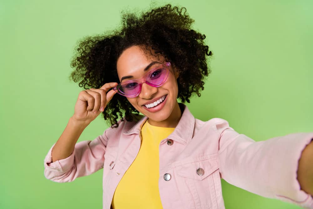 A cute black female with curly dry hair used a deep conditioner on her wet hair to make her hydrated hair stretchy.