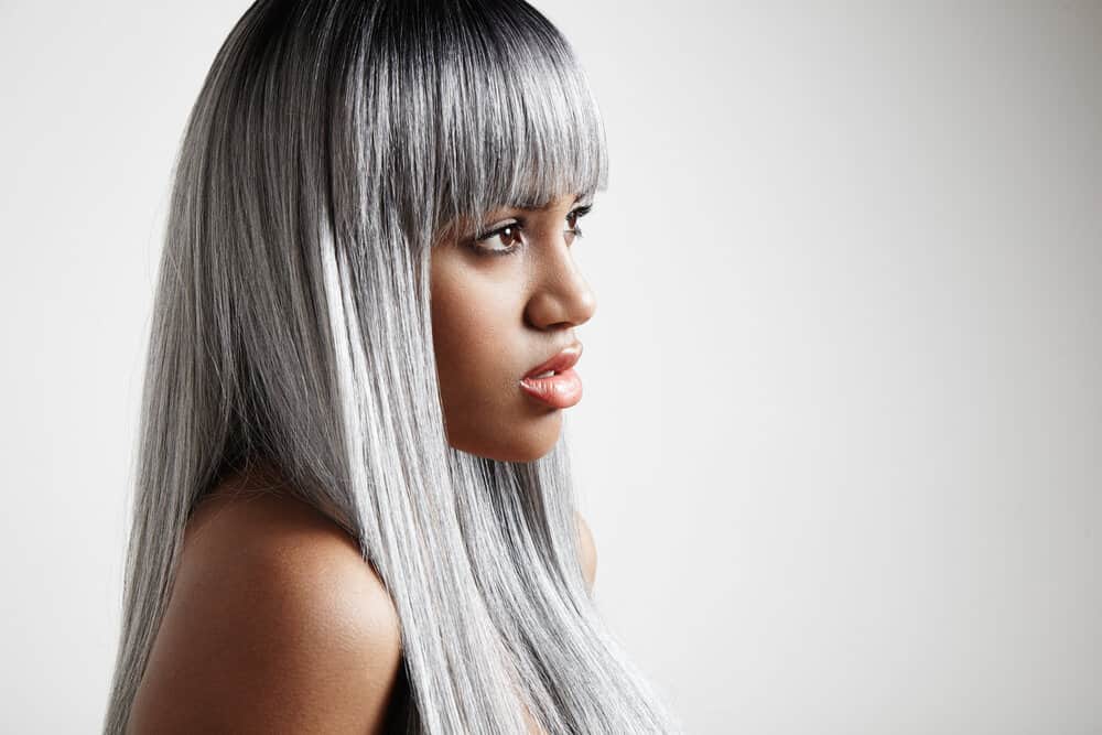 A black woman with dark brown natural hair color is starting to get naturally gray hair on her straightened long hair.