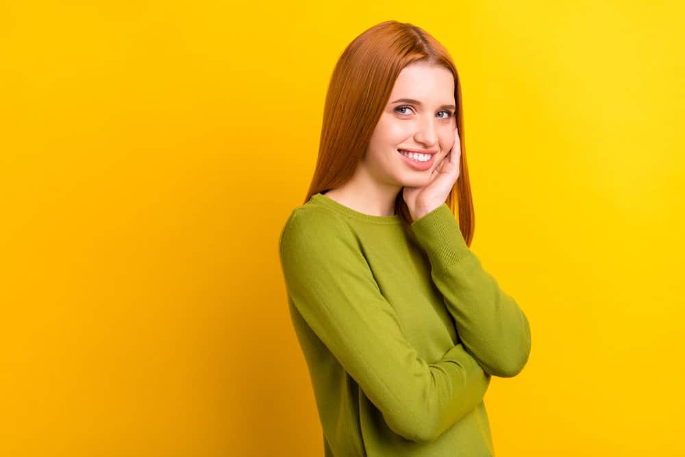 A young white woman in a green sweater has fine hair styled with Curly Girl-approved hair products.