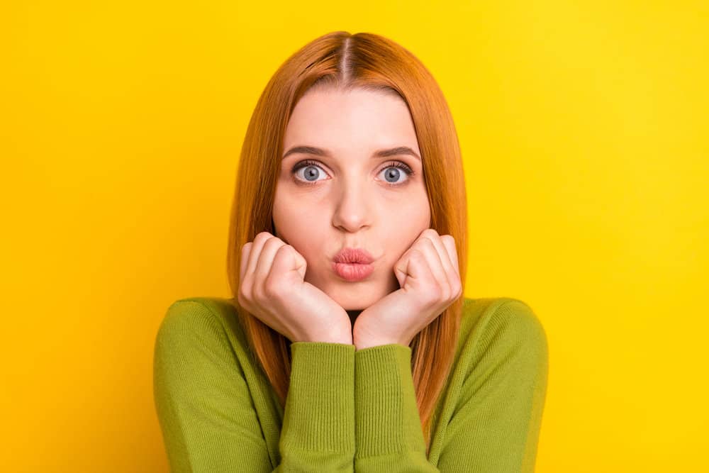 An attractive white female with gentle waves and a defined body on 1B hair strands is wearing a green sweater.