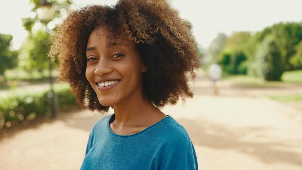 A young smiling woman with frizzy hair is wearing a classic wash-n-go style on her 4A African American hair type.