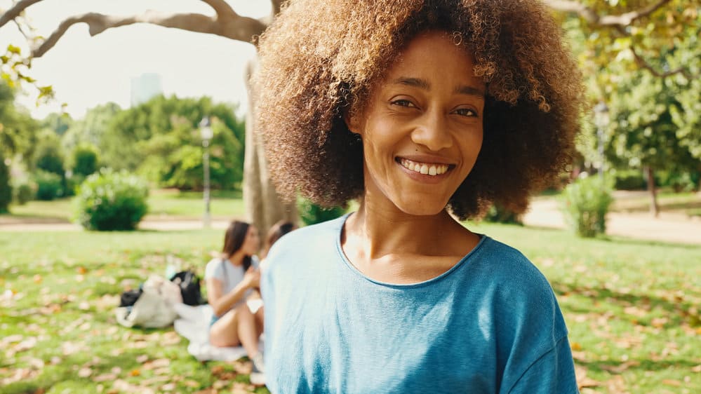 A happy black woman with high hair porosity wearing a wash-n-go which is one of our favorite curly hairstyles.