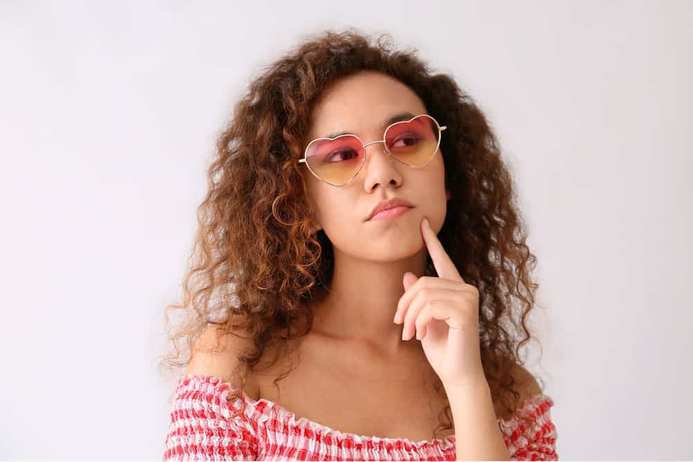 A thoughtful African-American female with a coarser hair texture used a blow dryer style dry and style her wet hair.