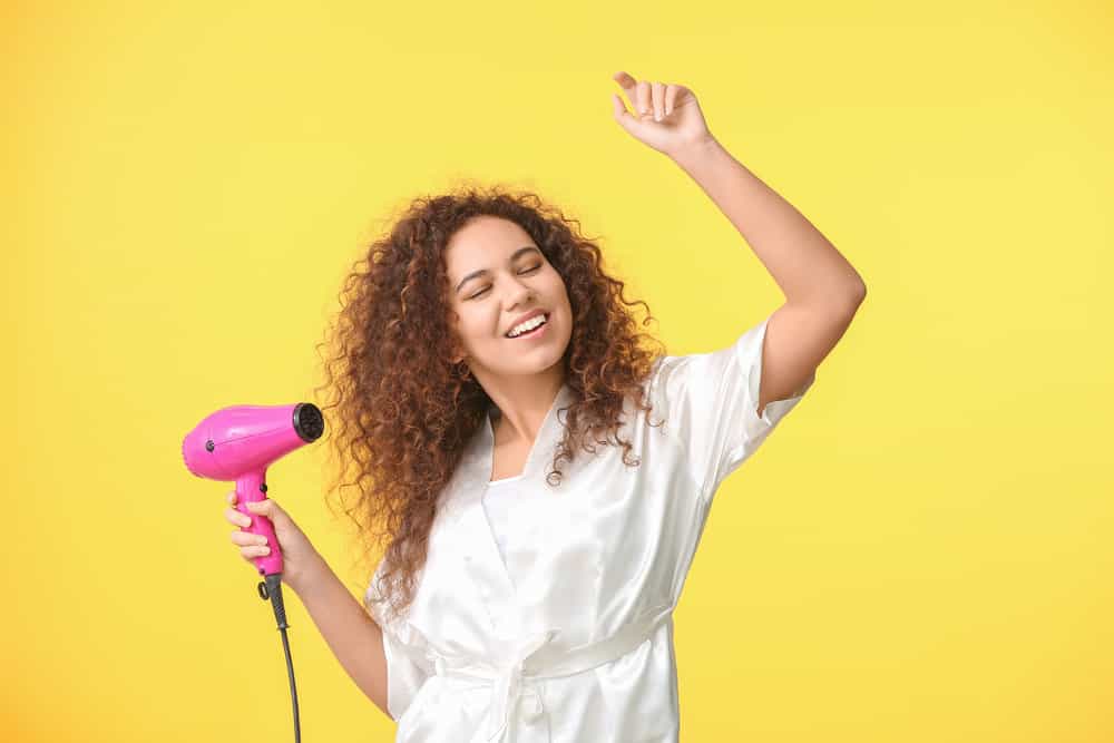 A young black lady with thinner hair planning to use a hair dryer on medium heat with concentrated airflow.