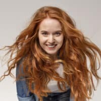 A cute red head with 2B hair strands using the Curly Girl method for a proper hair care routine for her wavy strands.