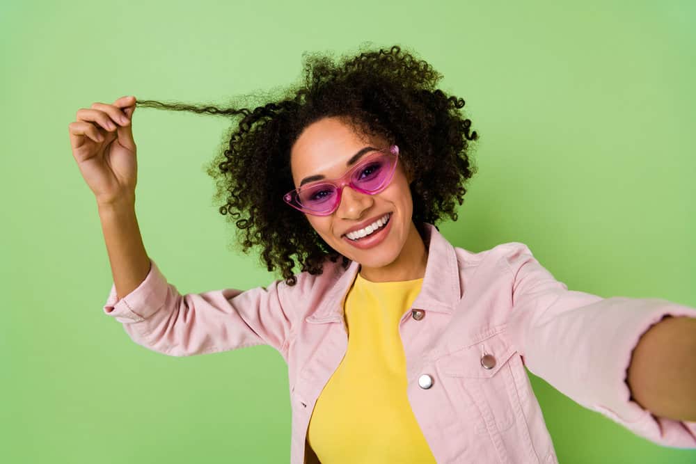 Stylish light-skinned black lady holding a dry hair shaft that needs to add moisture to improve hair elasticity.