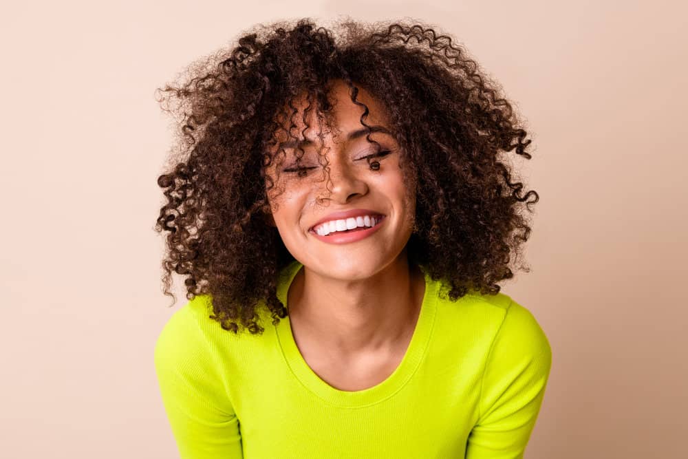 A cute curly girl with frizzy hair washed with mimosa flower shampoo, a leave-in smoothie cream, and coconut water.