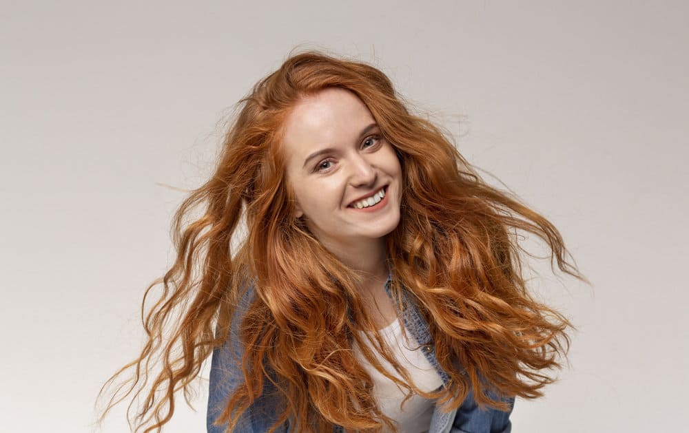 Female with a beautiful natural hair texture has red hair styled with argan oil and a Curly Girl approved styling cream.