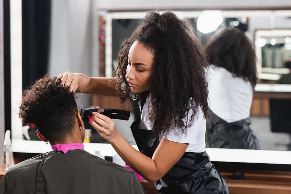 A young senior stylist that usually works at student salons is doing a live hair-cutting demonstration for students.