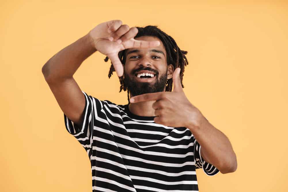 A cheerful African American guy with mature dreads on 4B curly hair follicles cleaned with natural hair care products.