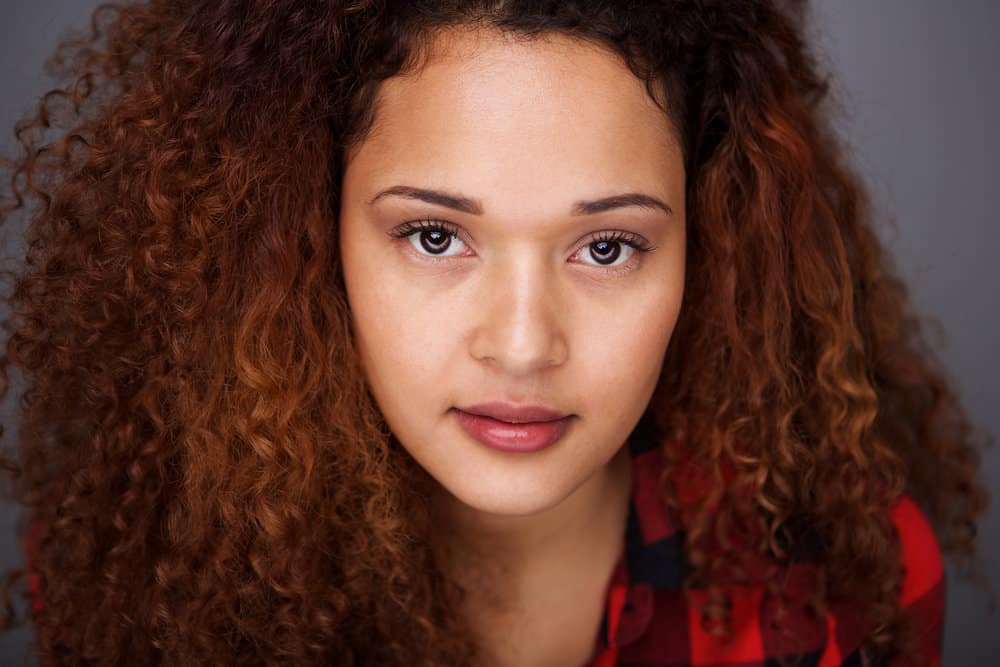 A young Hispanic woman wearing a DIY semi-permanent hair color on her naturally curly hair strands.