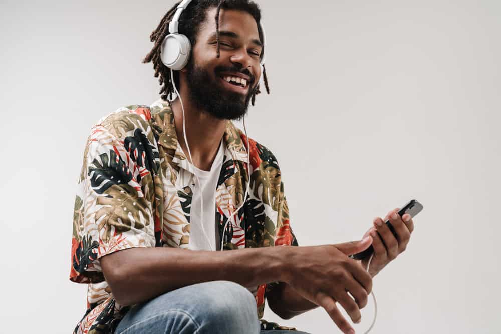 A positive young African American male wearing a colorful shirt is researching hair loss on his iPhone.