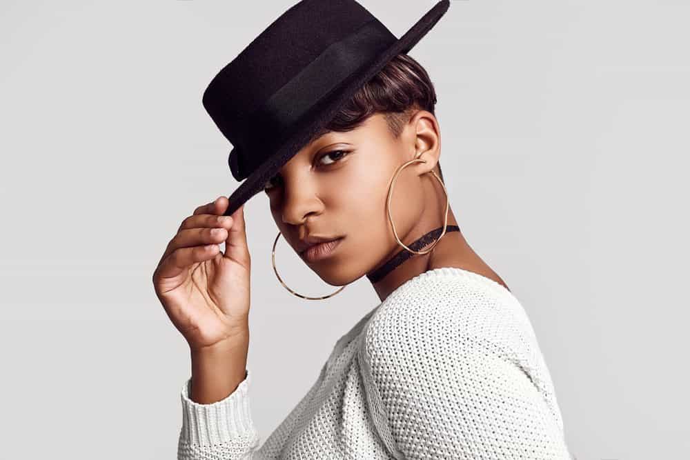A young hipster female with a combination of dark skin tones wearing gold hoop earrings and a black wide-brim hat.