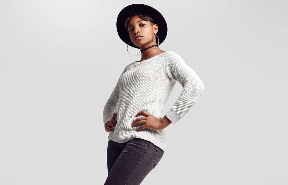 A very pretty female with a beautiful skin glow wearing a gray sweater and black jeans.