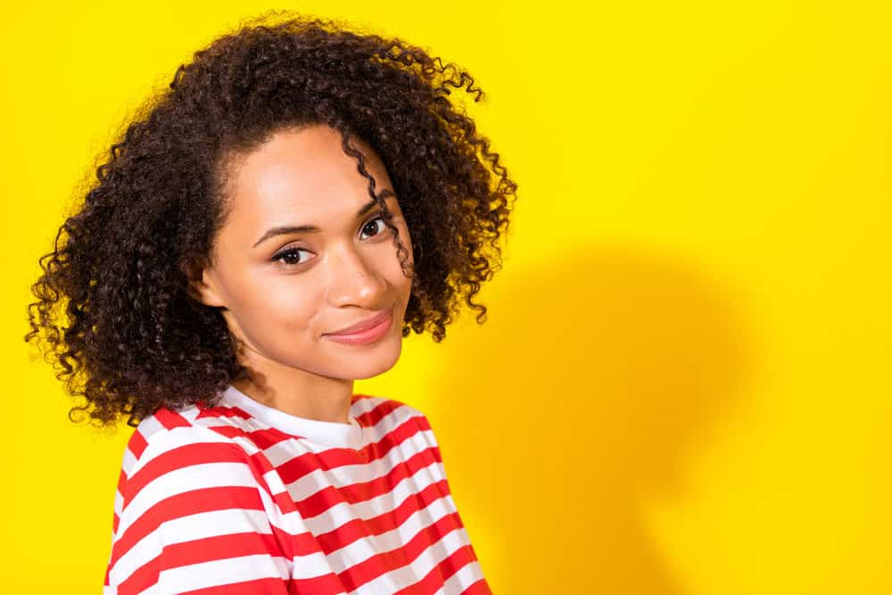 A cute black female washed her wet hair with a sulfate-free shampoo and styled it with cruelty-free black seed oil.