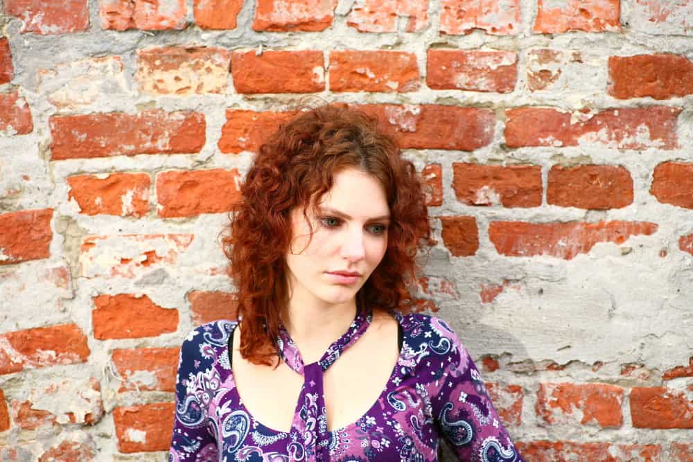 A closeup of a white female wearing a colorful purple dress with her 3b curls dyed red is leaving the hair salon.