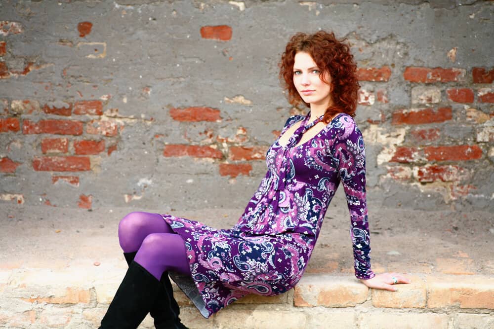 A young lady with shoulder-length curls sitting outside a brick wall showing off her loose spirals.