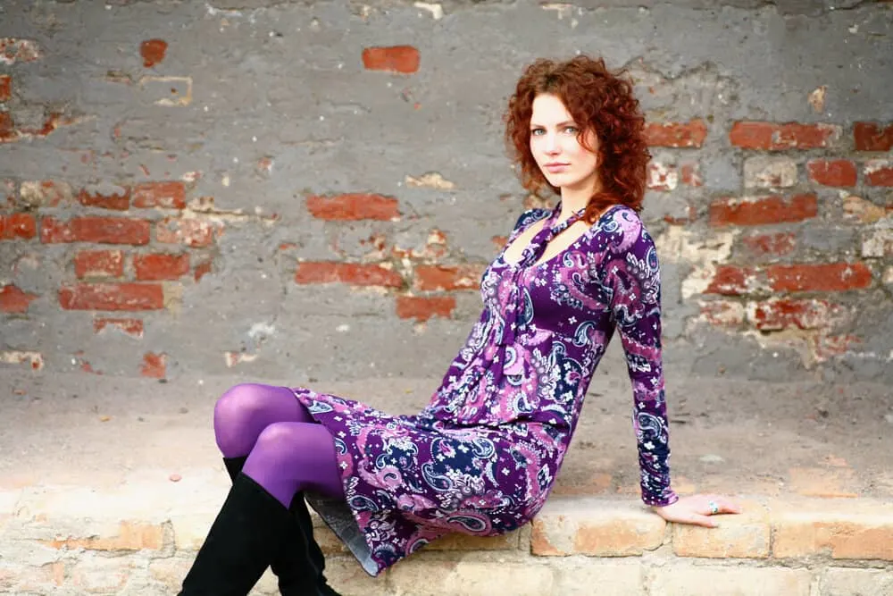 What Is 3A Hair? How To Take Care of It, Styles, and Products 12 A young lady with shoulder-length curls sitting outside a brick wall showing off her loose spirals.