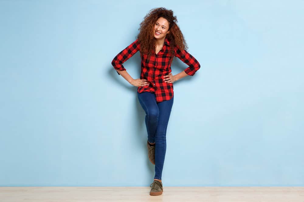 A female wearing a casual plaid shirt and blue jeans with dark brown curly hair colored with semi-permanent hair dye.